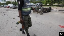 A Nigerian police officer walks past the burnt out shell of a car, after a car bomb exploded in Abuja, Nigeria, 1 Oct 2010