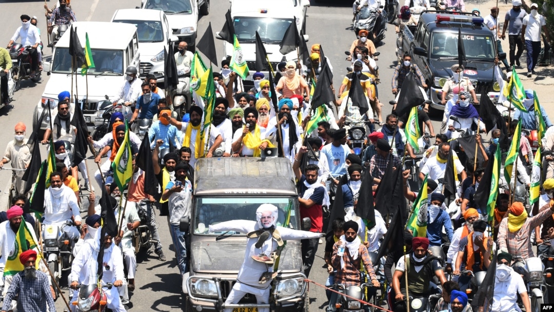 Para petani membawa bendera hitam mengendarai sepeda motor, mengiringi mobil yang menampilkan patung Perdana Menteri India Narendra Modi, dalam unjuk rasa 'Hari Hitam' menandai enam bulan aksi protes reformasi pertanian di Amritsar, India, 26 Mei 2021. (NARINDER NANU / AFP)