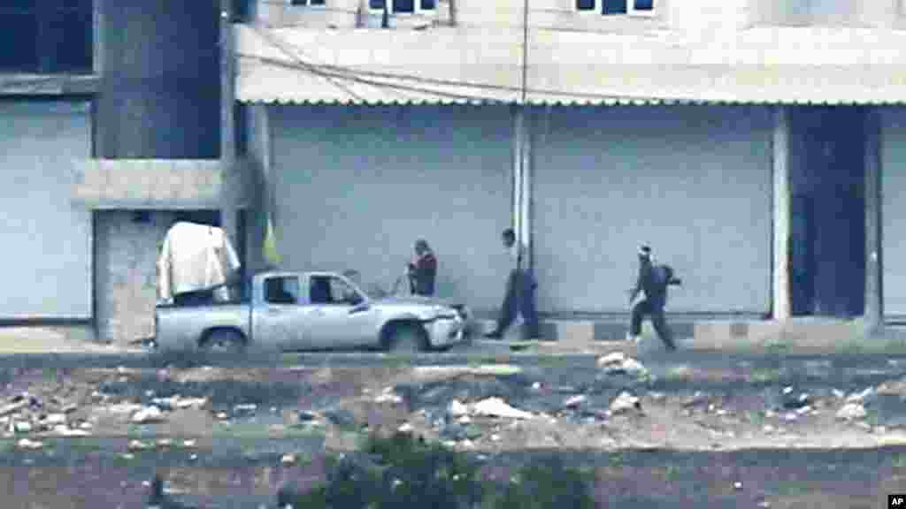 In this photo shot with an extreme telephoto lens and through haze from a hilltop in Mursitpinar on the outskirts of Suruc at the Turkey-Syria border, Kurdish fighters walk to their positions next to a machine-gun-fitted pickup truck, in Kobani, Syria, Oc