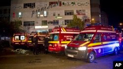 Ambulances are parked outside the site of an explosion that occurred in a club, housed by the building in the background, in Bucharest, early Saturday, Oct. 31, 2015.