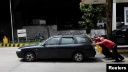 Empleados de una gasolinera empujan un auto en Caracas.