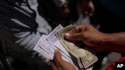 Un vendedor cuenta bolívares y dólares estadounidenses para entregar cambio a un cliente en un mercado público en el barrio de Petare en Caracas, el 18 de enero de 2022. Foto: AP.