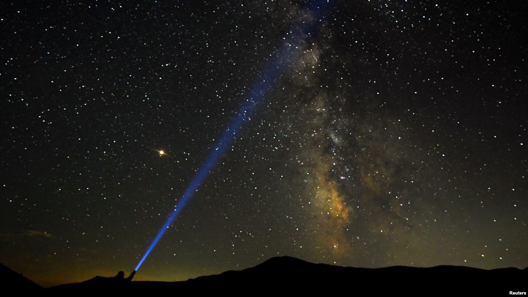 Seorang pria menyorot lampu ke arah Milky Way saat puncak hujan meteor Perseid di Taman Nasional Mavrovo, di Macedonia, 12 Agustus 2018. (Foto: Reuters)