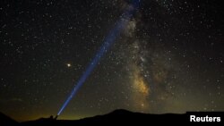 Seorang pria menyorot lampu ke arah Milky Way saat puncak hujan meteor Perseid di Taman Nasional Mavrovo, di Macedonia, 12 Agustus 2018. (Foto: Reuters)