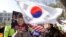 A supporter of impeached South Korean President Park Geun-hye waves flags of the U.S. and South Korea while another holds a portrait of the president during a rally opposing her impeachment in Seoul, South Korea, Feb. 27, 2017. 