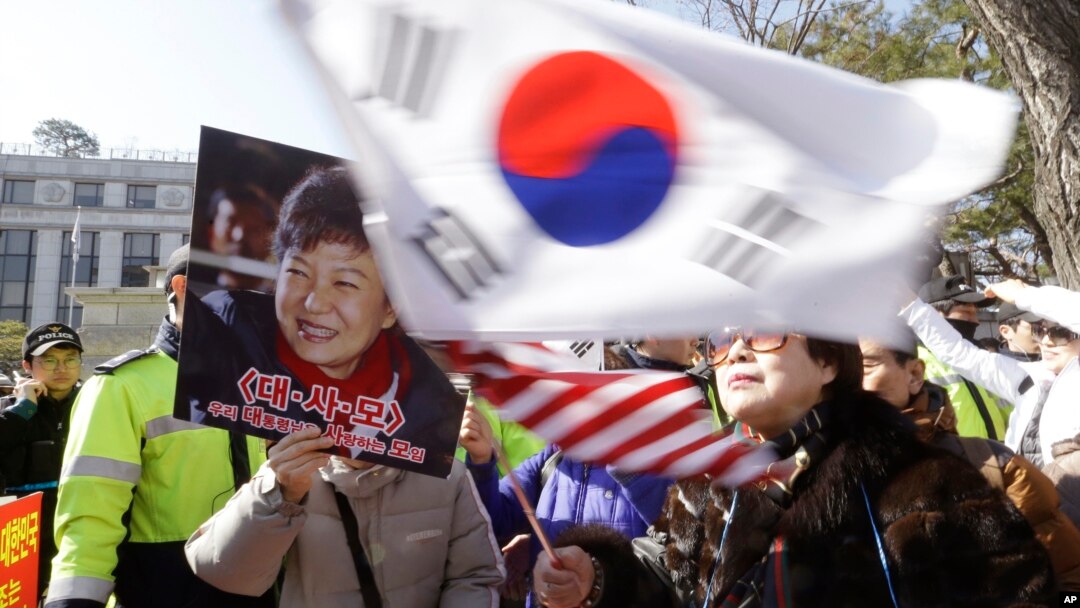 A supporter of impeached South Korean President Park Geun-hye waves flags of the U.S. and South Korea while another holds a portrait of the president during a rally opposing her impeachment in Seoul, South Korea, Feb. 27, 2017. 