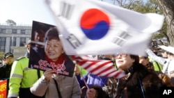 A supporter of impeached South Korean President Park Geun-hye waves flags of the U.S. and South Korea while another holds a portrait of the president during a rally opposing her impeachment in Seoul, South Korea, Feb. 27, 2017. 