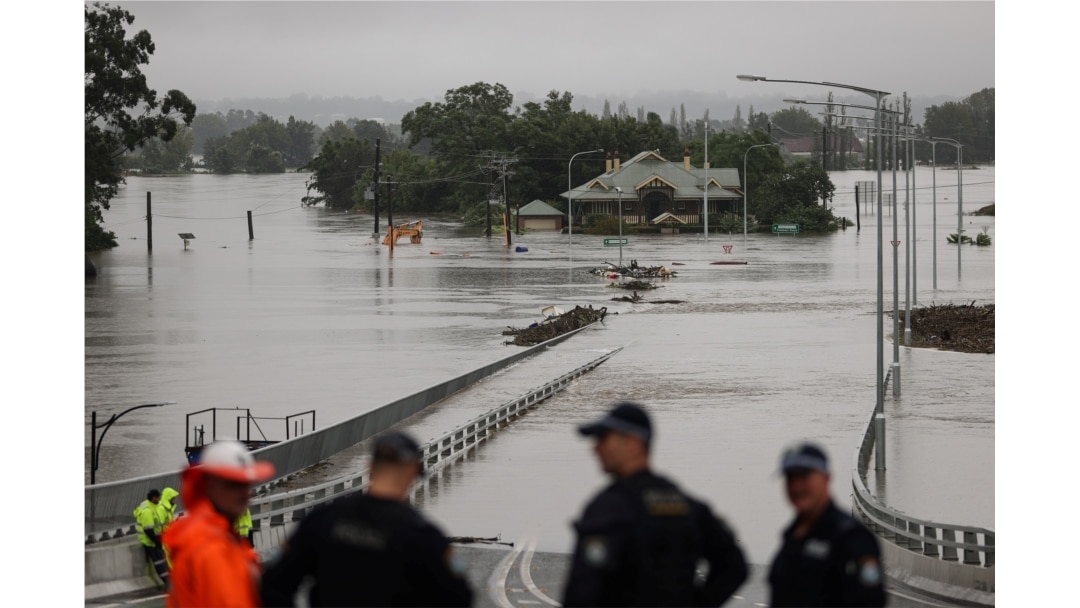Police officers and road workers are seen in front of a submerged structure visible in floodwaters in the suburb of Windsor in Sydney, Australia, March 22, 2021.