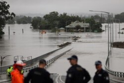 Police officers and road workers are seen in front of a submerged structure visible in floodwaters in the suburb of Windsor in Sydney, Australia, March 22, 2021.