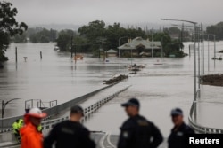 Police officers and road workers are seen in front of a submerged structure visible in floodwaters in the suburb of Windsor in Sydney, Australia, March 22, 2021.