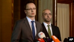 Hungarian Foreign Minister Peter Szijjarto, with government spokesman Zoltan Kovacs at right, talks to reporters in Budapest about plans to build a fence along the Hungarian-Serbian border to try to stop migrants from entering, June 17, 2015.