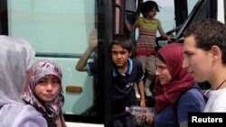 FILE - A group of migrants prepare to leave for a different camp, at a makeshift camp for refugees and migrants at the Greek-Macedonian border near the village of Idomeni, Greece, May 11, 2016. 