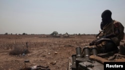 An SPLA tank drives past the remains of a rebel soldier killed near Bor on January 26, 2014, days after a peace deal was signed. South Sudan opposition forces accused the government of fresh attacks at the weekend, including on the hometown in Unity state of former vice president Riek Machar. REUTERS/George Philipas 