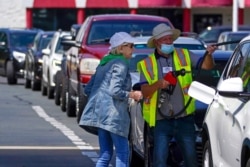 FILE - A customer helps pump gas at Costco, as others wait in line, in Charlotte, N.C., May 11, 2021.