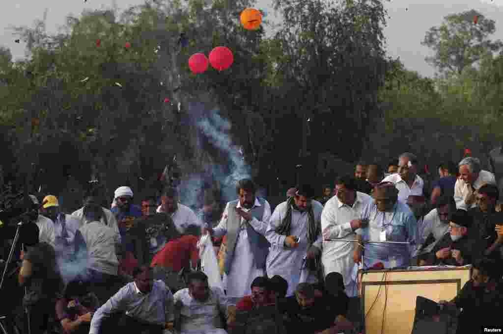 Men and supporters react after a bunch of balloons burst in the air on-stage where Mohammad Tahir ul-Qadri (R, on table), Sufi cleric and leader of political party Pakistan Awami Tehreek (PAT), was addressing the crowd during the Revolution March in Islamabad.