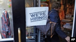 FILE - In this May 18, 2016, file photo, a woman passes a "We're Hiring!" sign while entering a clothing store in the Downtown Crossing of Boston. 