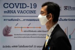 A man wearing a face mask stands next to a board showing the progress of developing an mRNA type vaccine candidate for COVID-19 during a news conference at the National Primate Research Center of Chulalongkorn University, June 22, 2020.