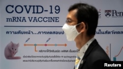 A man wearing a face mask stands next to a board showing the progress of developing an mRNA type vaccine candidate for COVID-19 during a news conference at the National Primate Research Center of Chulalongkorn University, June 22, 2020. 