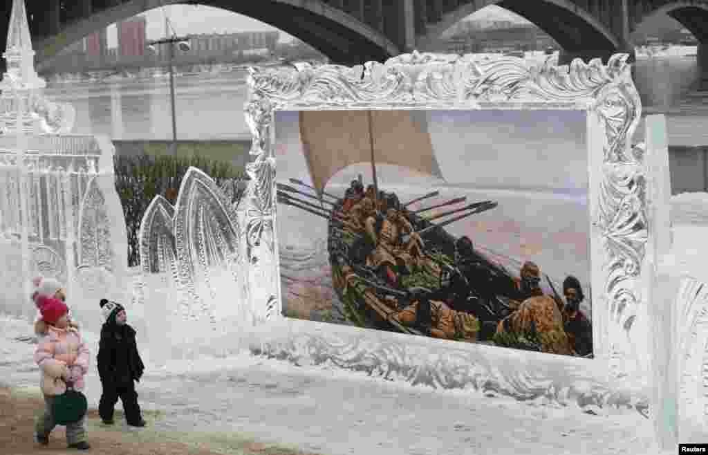 Tiga orang anak melewati sebuah lukisan reproduksi karya pelukis Rusia, Vasily Surikov yang dipamerkan dengan pigura es dalam Festival Seni di Krasnoyarsk, Siberia, Rusia. 