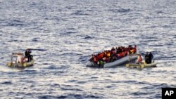 Photo provided by the Italian Navy shows rescue crews approaching migrants on a rubber boat some 40 miles (65 kilometers) from the Libyan capital, Tripoli.