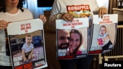 FILE -Ofri Bibas Levy, whose brother Yarden (34) was taken hostage with his wife Shiri (32) and 2 children Kfir (10 months) and Ariel (4), holds with her friend Tal Ulus pictures of them during an interview with Reuters, in Geneva, Switzerland, November 13, 2023.