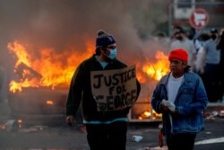 A man wearing a face mask holds a sign near a burning vehicle at the parking lot of a Target store on May 28, 2020, during protests after a black man died in police custody in Minneapolis, Minn.