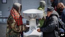 Visitors waiting to collect free food outside the Bowery Mission are instructed to wash their hands at a kiosk due to coronavirus concerns, April 1, 2020, in New York.