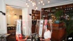 A man and a woman demonstrate dining under a plastic shield, May 27, 2020 in a restaurant of Paris.