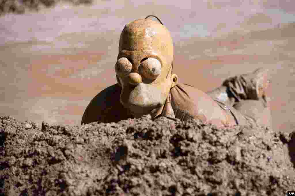 A participant of the traditional dirty pig festival wearing a Homer Spimpson mask wallows in a slough near Hergisdorf, Germany, May 25, 2015.