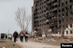 Orang-orang berjalan di dekat blok flat, yang hancur selama konflik Ukraina-Rusia di kota pelabuhan selatan yang terkepung Mariupol, Ukraina 17 Maret 2022. REUTERS/Alexander Ermochenko