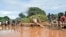 FILE - Residents of Chamwana Muma village walk through flood water after using a makeshift bridge to cross the swollen River Tana, in Tana Delta, Kenya, on Wednesday Nov. 15, 2023.