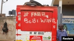 A man leans on a closed kiosk with graffiti calling to free Ugandan opposition presidential candidate Bobi Wine, in Kampala, Uganda, Jan. 17, 2021. 