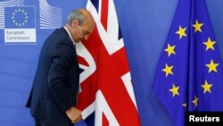 FILE - A worker arranges flags at the EU headquarters as Britain and the EU launch Brexit talks in Brussels, June 19, 2017. 