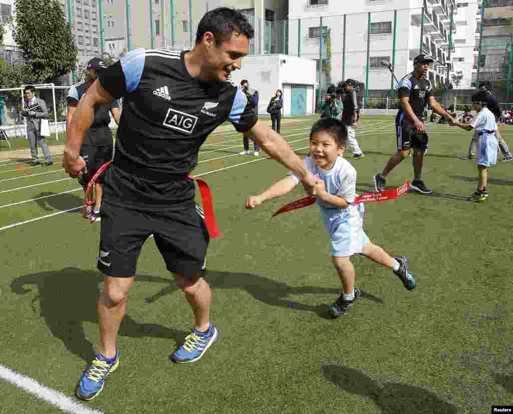 Pemain  Tim All Blacks' dari Selandia Baru, Daniel Carter, tampak bermain bersama seorang murid dalam kunjungan Tim All Blacks ke SD Aoyama menjelang pertandingan persahabatan rugby internasional  antara Selandia Baru dan Jepang hari sabtu di Tokyo.