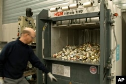 In this image provided by Comite Champagne, a worker prepares to press the button of a machine to crush empty Miller High Life beer cans at the Westlandia plant in Ypres, Belgium on April 17, 2023. (Comite Champagne via AP)