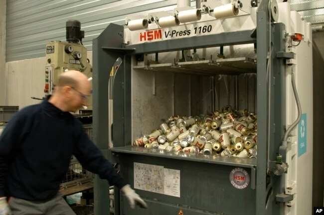 In this image provided by Comite Champagne, a worker prepares to press the button of a machine to crush empty Miller High Life beer cans at the Westlandia plant in Ypres, Belgium on April 17, 2023. (Comite Champagne via AP)