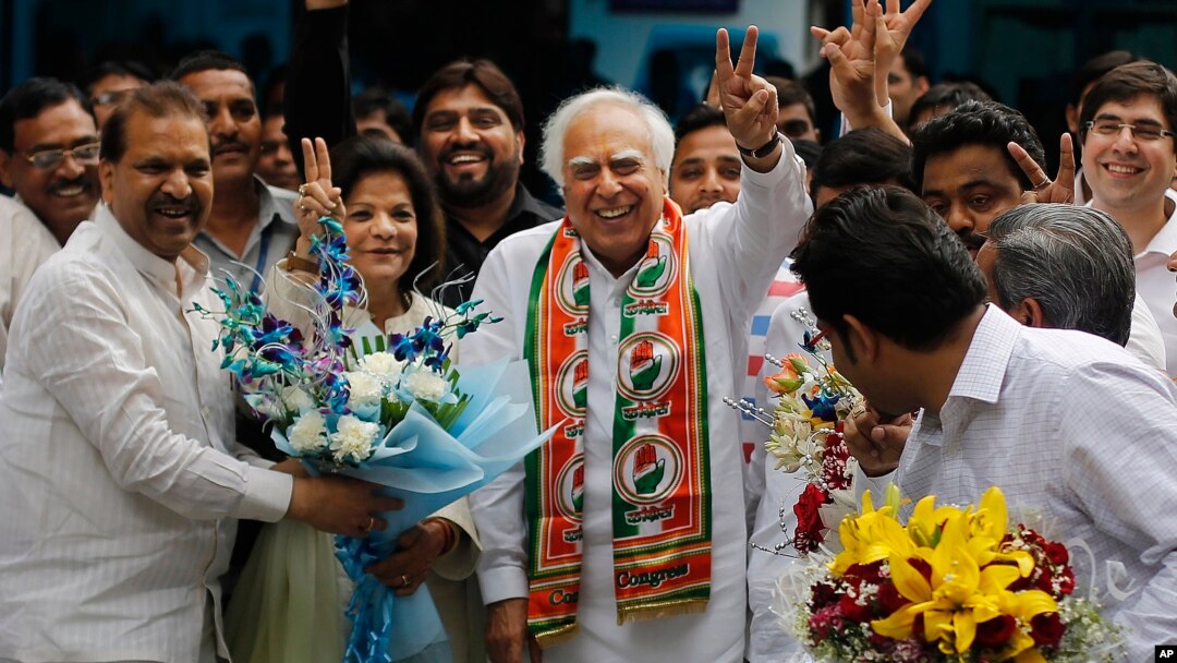 Congress party leader Kapil Sibal, center and his wife Promila Sibal flash victory signs as supporters present them with flower bouquets after Sibal filed his nomination papers for the upcoming parliamentary elections in New Delhi, India, March 20, 2014.
