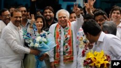 Congress party leader Kapil Sibal, center and his wife Promila Sibal flash victory signs as supporters present them with flower bouquets after Sibal filed his nomination papers for the upcoming parliamentary elections in New Delhi, India, March 20, 2014.