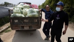 In this April 6, 2020 photo, volunteer Luo Hao, right, talks about his work near a farmer with his harvest of vegetable to be collected by other volunteers in Wuhan in central China's Hubei province.