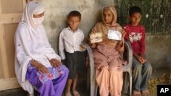 Pakistan's Noor Bibi, second from right, shows pictures of her husband and son whom she alleges were picked up by security agencies last week as she sits with unidentified family members in Abbottabad, Pakistan, June 15, 2011