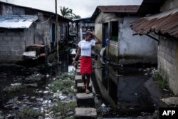 FILE - A woman walks over blocks to keep out of the stagnant water in Clara town, Monrovia on October 4, 2023.