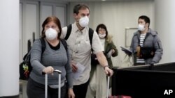 Para calon penumpang mengenakan masker saat berjalan melalui terminal 5 di bandara internasional O'Hare, Chicago, AS, 1 Maret 2020. (AP Photo/Nam Y. Huh)