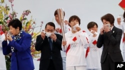 Tokyo Gov.Yuriko Koike, left, Tokyo 2020 Organizing Committee President Seiko Hashimoto, right, and attendees take off face masks to pose for group photos during the Tokyo 2020 Olympic Torch Relay Grand Start in Naraha, Fukushima, Japan, March 25, 2021.