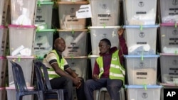 Electoral workers sit next to stacked ballot boxes after they were received at a tallying center in Nairobi, Kenya, Thursday, Aug. 11, 2022. Kenyans are waiting for the results of a close presidential election in which the turnout was lower than usual.