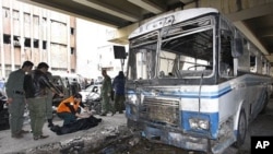 Two Syrian security men, left, look to a civil defense worker as he checks a dead body, next to a damaged riot police forces bus at the scene of a suicide bomb attack, at Midan neighborhood, in Damascus, Syria, on Friday Jan. 6, 2012.