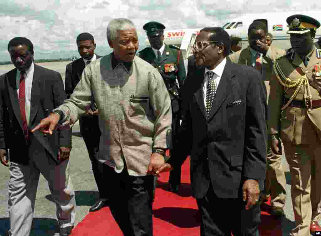 President Nelson Mandela, left, walks hand in hand with Zimbabwean President Robert Mugabe after the South African leader's arrival in Harare to address the 8th Assembly of the World Council of Churches, December 13, 1998. (AP)