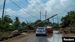 FOTO FILE: Mobil-mobil melaju di bawah tiang listrik yang tumbang setelah Badai Fiona di Santa Isabel, Puerto Rico 21 September 2022. (REUTERS/Ricardo Arduengo/File Foto)