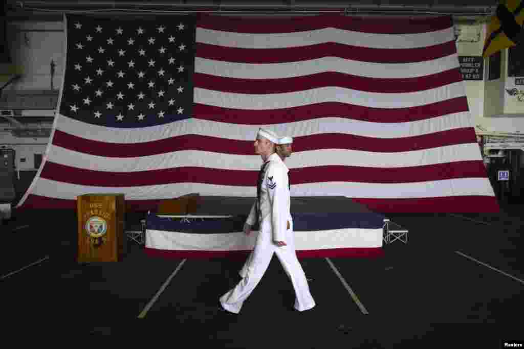 2013年4月15日，美国两栖攻击舰貝里琉号（USS Peleliu）上的美国国旗前面，两位水兵走过。当时正在香港进行例行港口访问的貝里琉号停泊在尖沙咀。