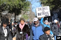 Seorang peserta pawai mengangkat plakat dalam unjuk rasa damai di South Carolina Statehouse untuk menghormati Martin Luther King Jr. di Columbia, South Carolina, Senin, 20 Januari 2025. (Jeffrey Collins/AP)