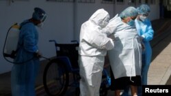 Una mujer es auxiliada tras ser dada de alta en el hospital en el que estuvo internada por complicaciones del coronavirus, en Santa Tecla, El Salvador.